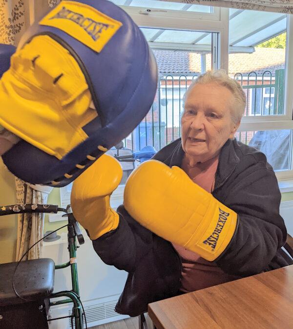 A lady called Dot, seated, wearing Boxing gloves and punching apunch bag