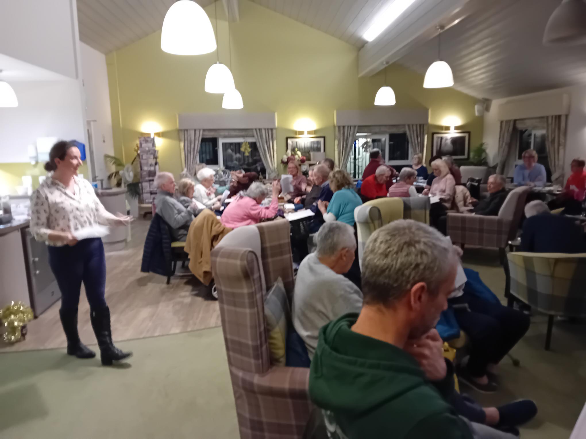 People sat at tables singing, with a woman at the front leading