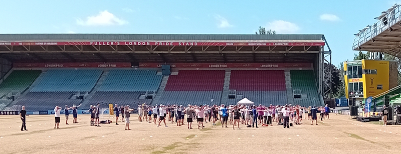 A large group of people exercising in front of the Fuller's Pride seating at the Stoop Stadium
